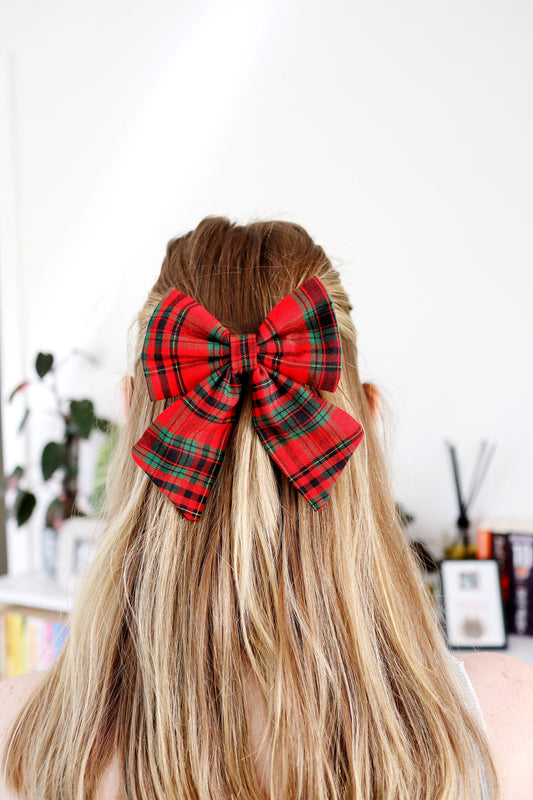 Red plaid hair bow on a person with long blonde hair, blurred indoor background