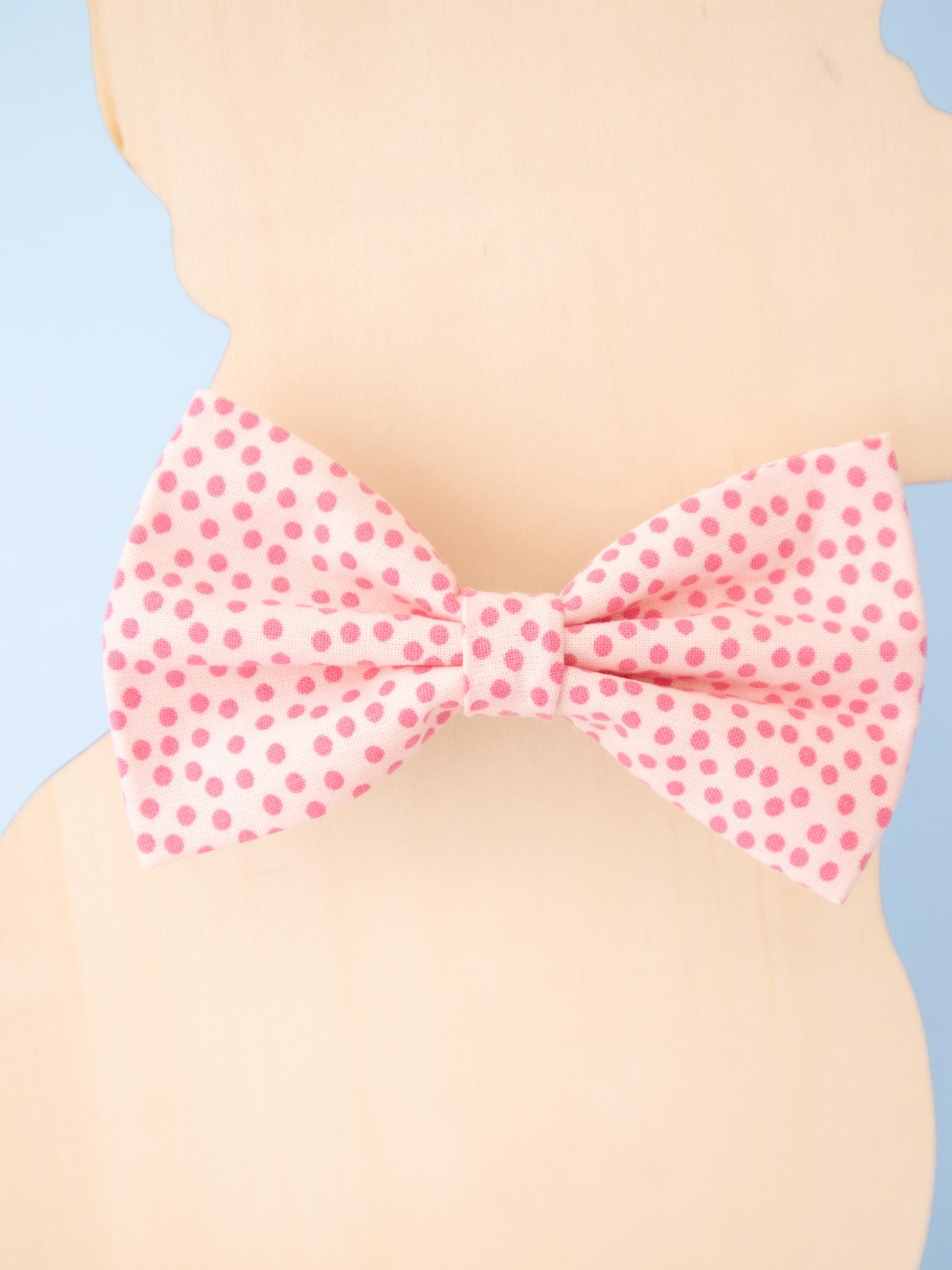 Pink polka dot bow tie on a dog model against a blue and beige background
