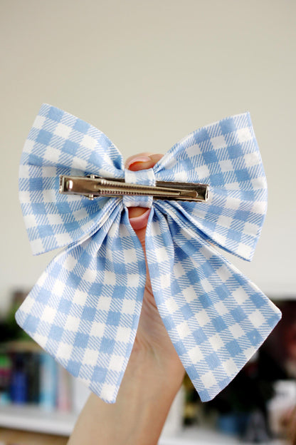 Blue and white checkered bow hair clip held by a hand against a blurred background