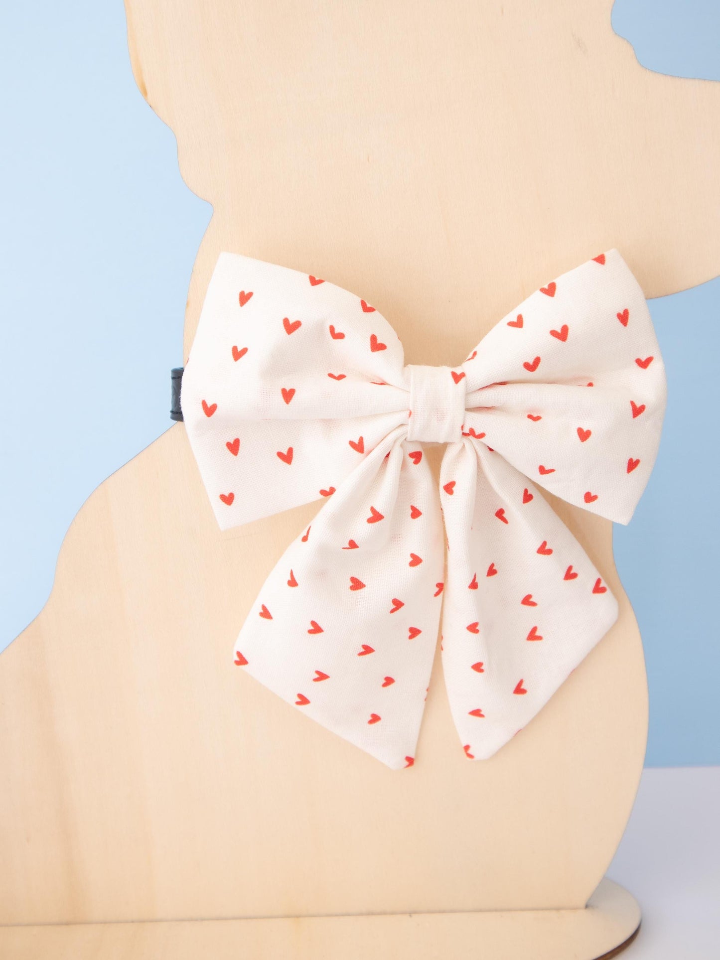 Dog Mannequin wearing a large white bow featuring red heart patterns against a light blue background.
