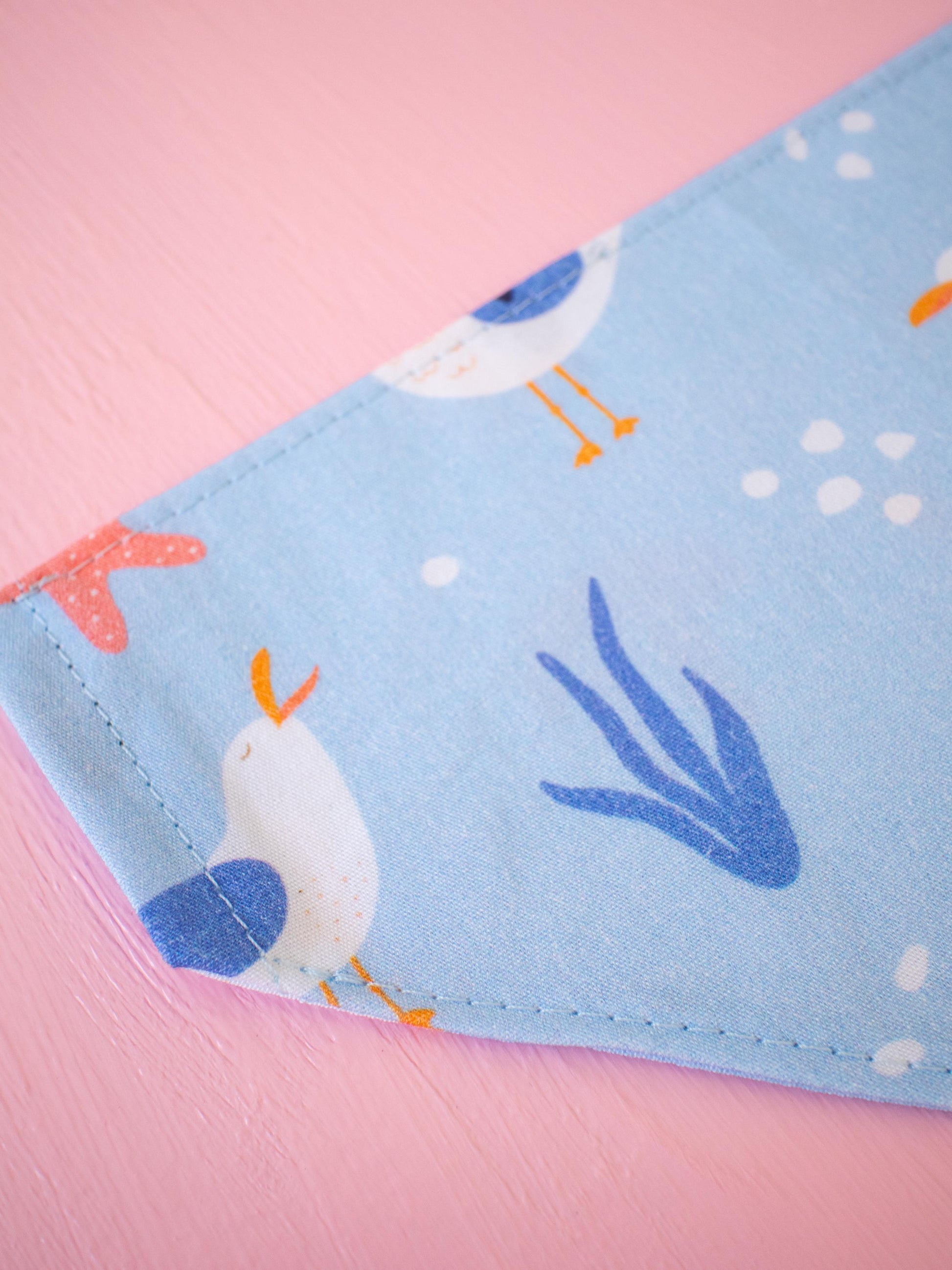 Close up of blue Dog bandana featuring seaweed, coral and seagulls on a pink background