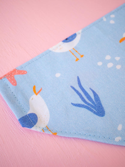 Close up of blue Dog bandana featuring seaweed, coral and seagulls on a pink background