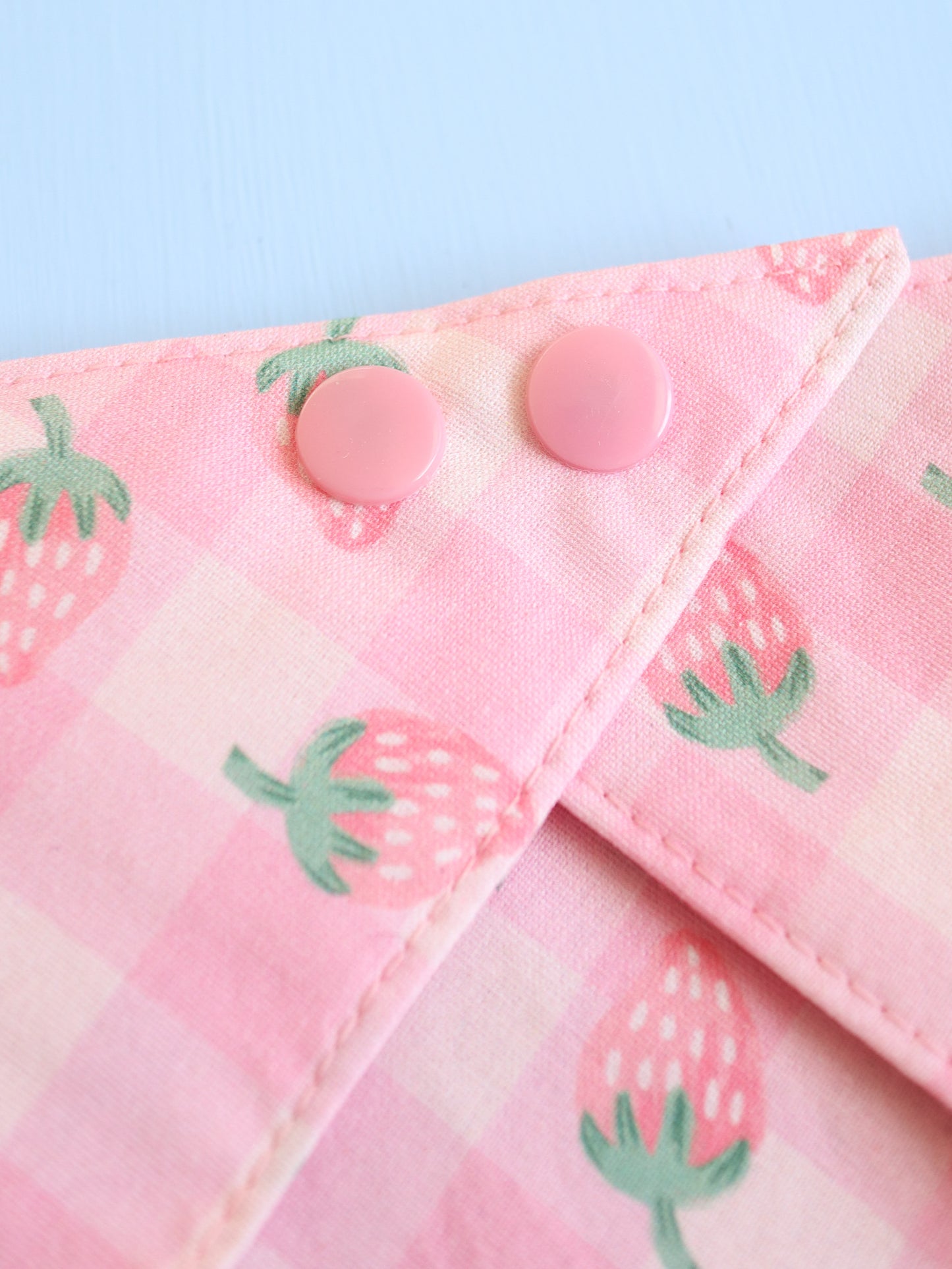 Close-up of a pink fabric with strawberry patterns and buttons on a light blue background