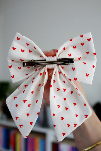 White bow with red heart patterns held by a hand against a blurred background