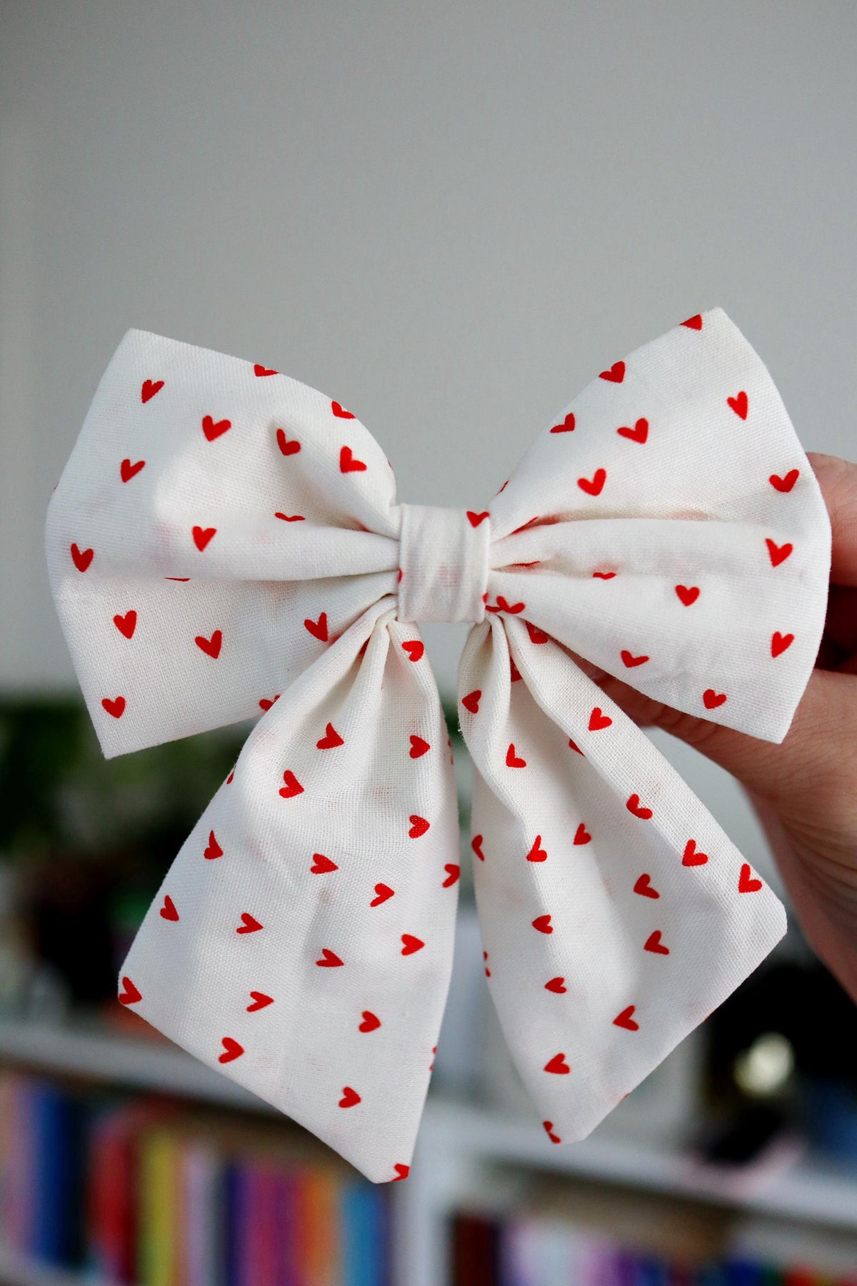 White bow with red heart patterns held against a blurred background