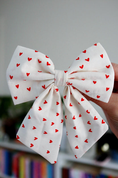 White bow with red heart patterns held against a blurred background
