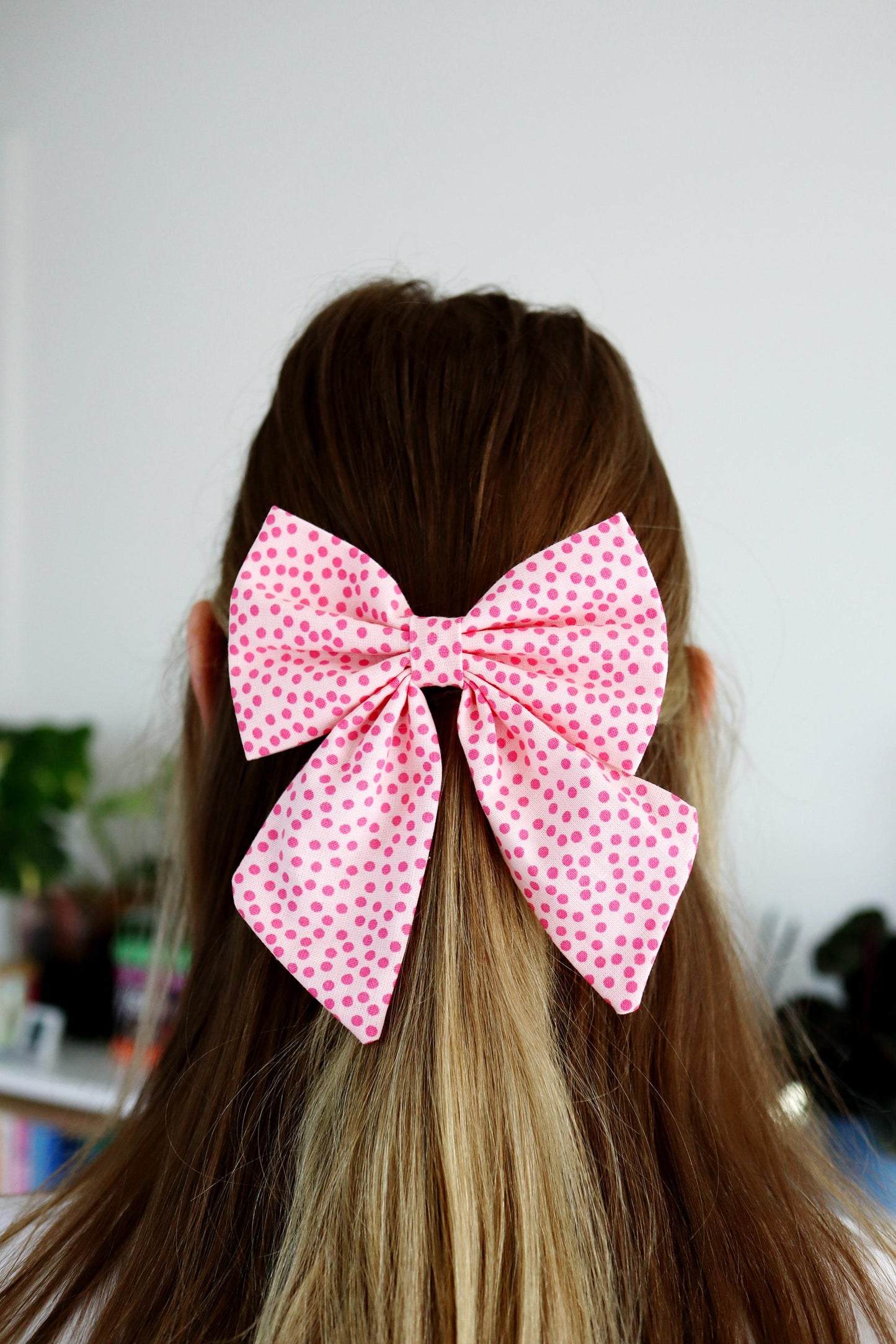 Person with pink polka dot bow in hair against a neutral background