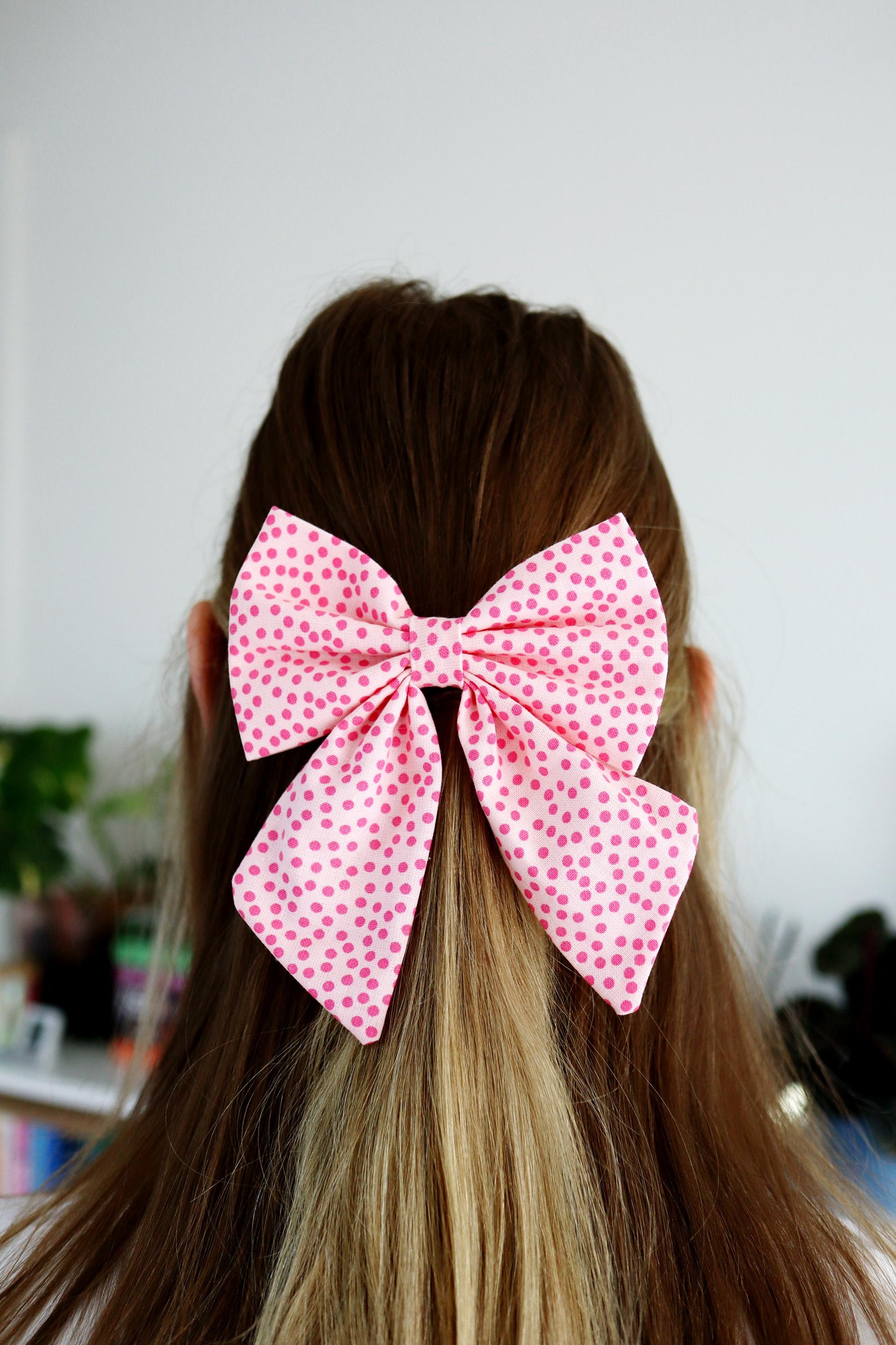 Person with pink polka dot bow in hair against a neutral background