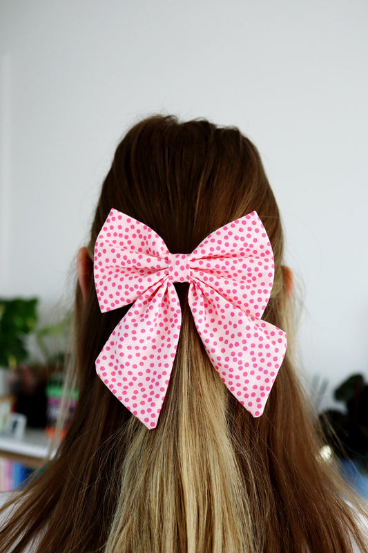 Person with pink polka dot bow in hair against a neutral background