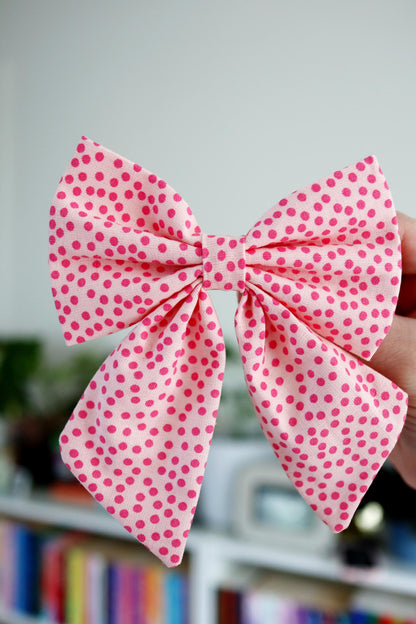 Pink polka dot bow held against a blurred background