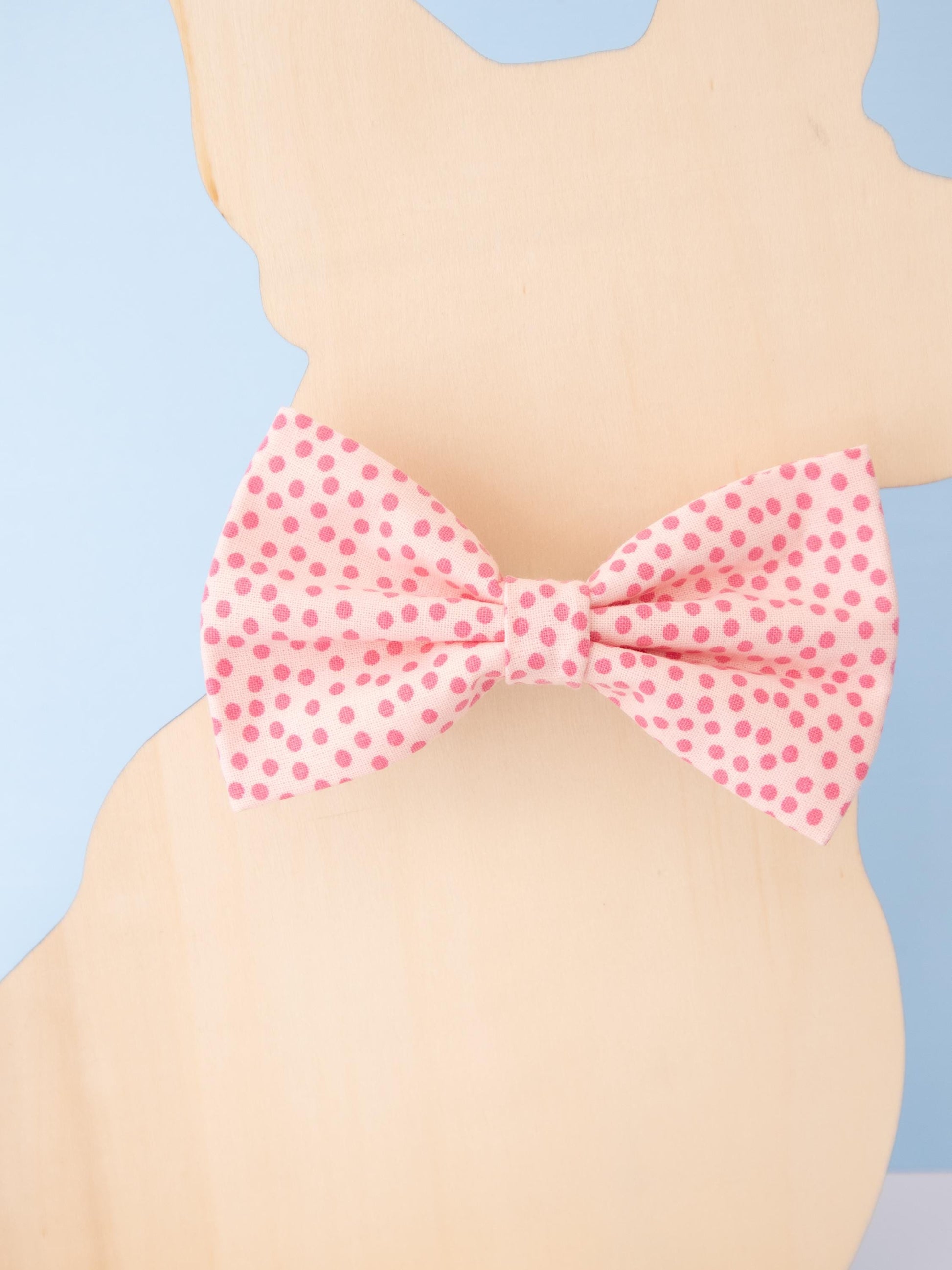 Pink polka dot bow tie on a dog model against a light blue background
