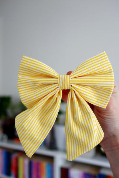 Yellow striped bow held in a hand with a blurred bookshelf background