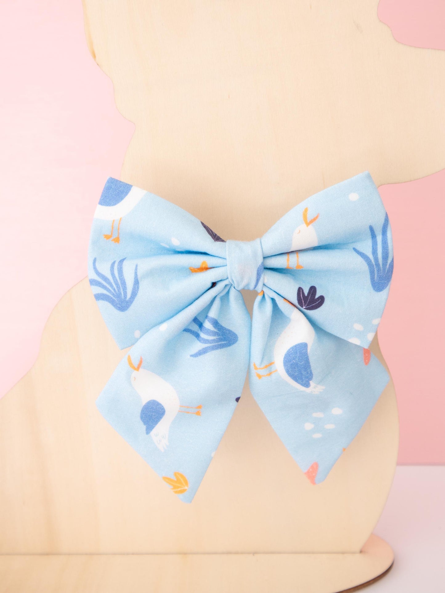 Large blue bow with cartoon seagull character design on a mannequin head against a pink background