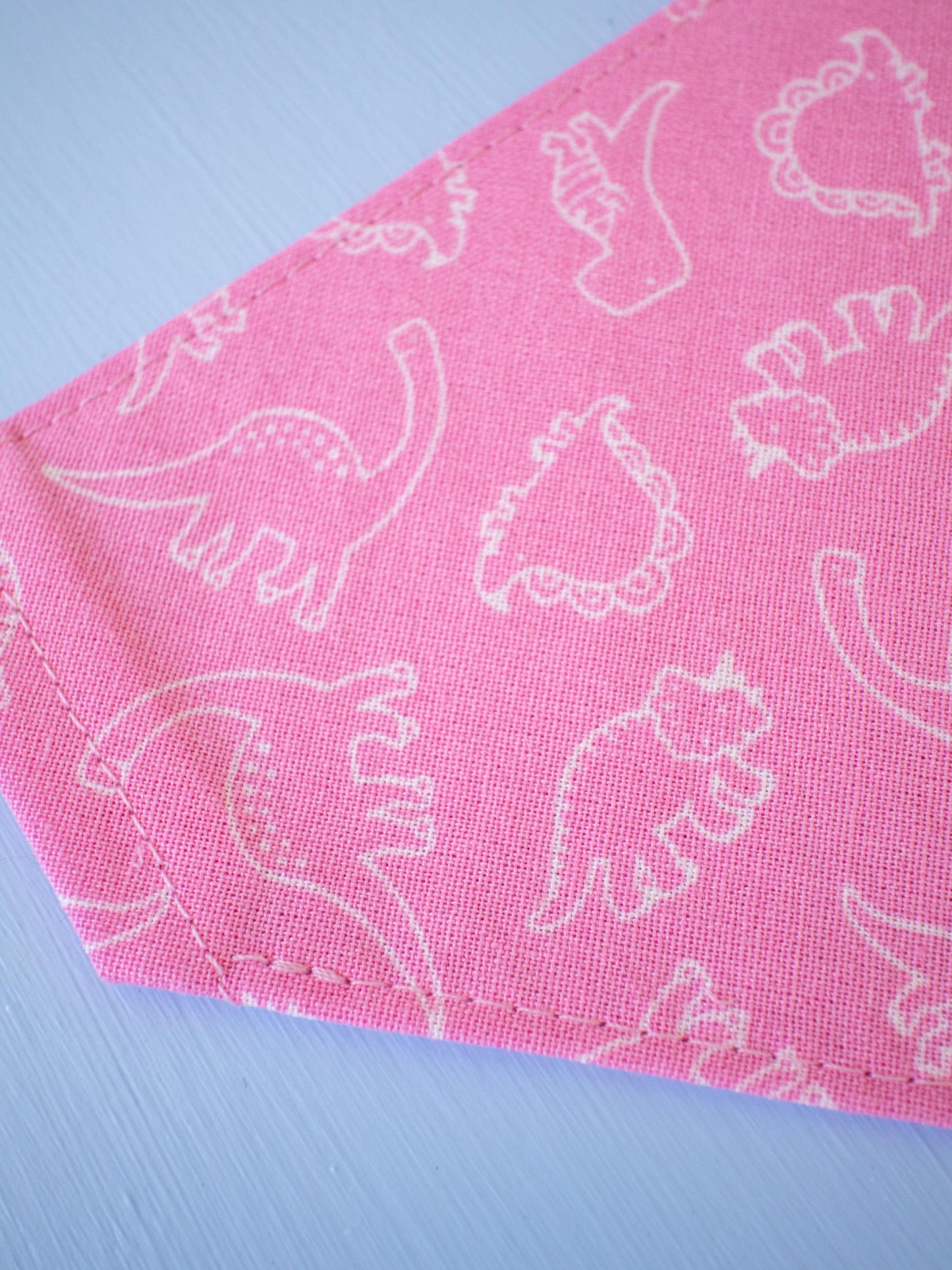 Pink fabric with white dinosaur patterns on a light blue background