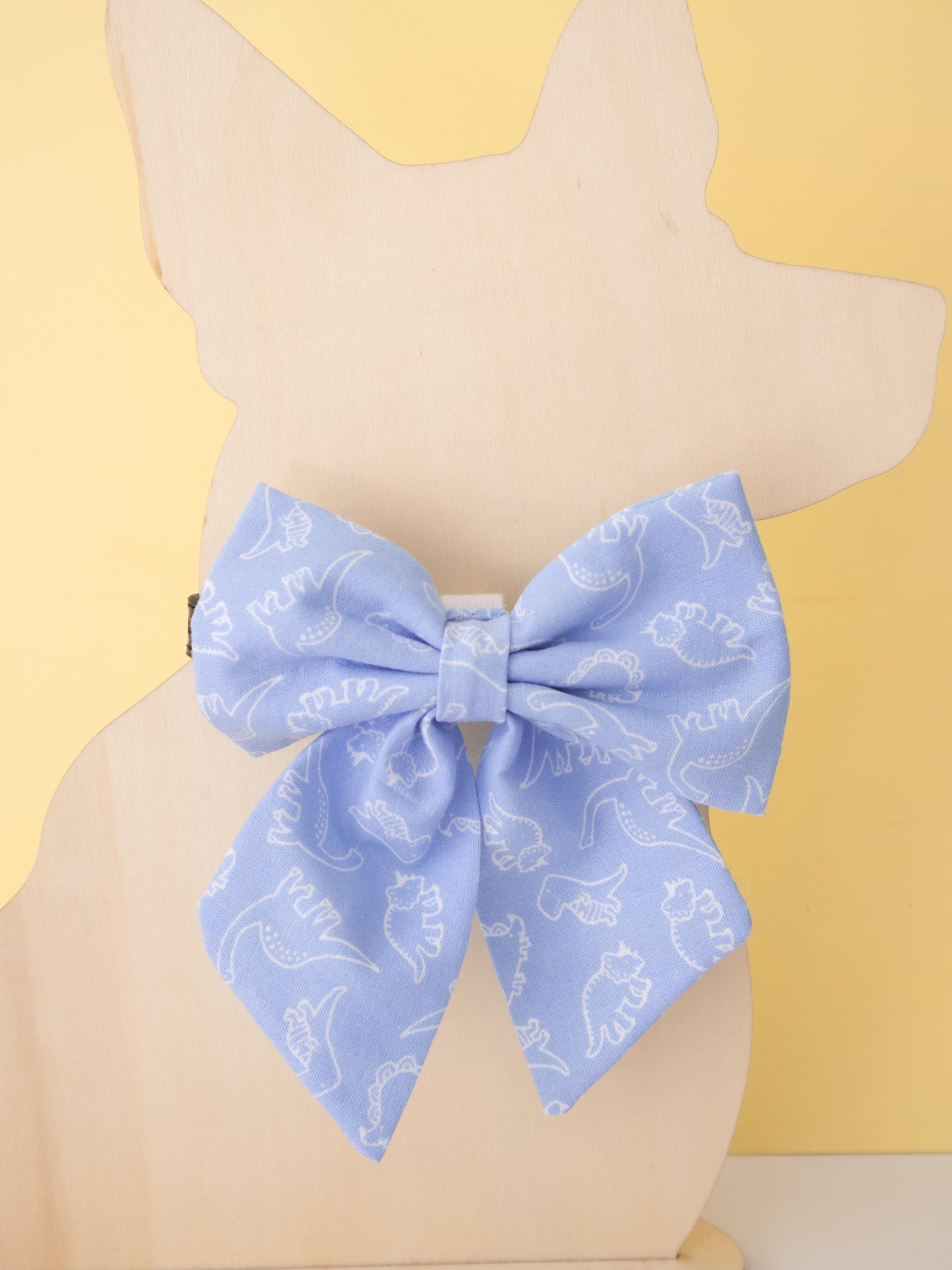 Blue bow with white dinosaur pattern on a mannequin against a yellow background