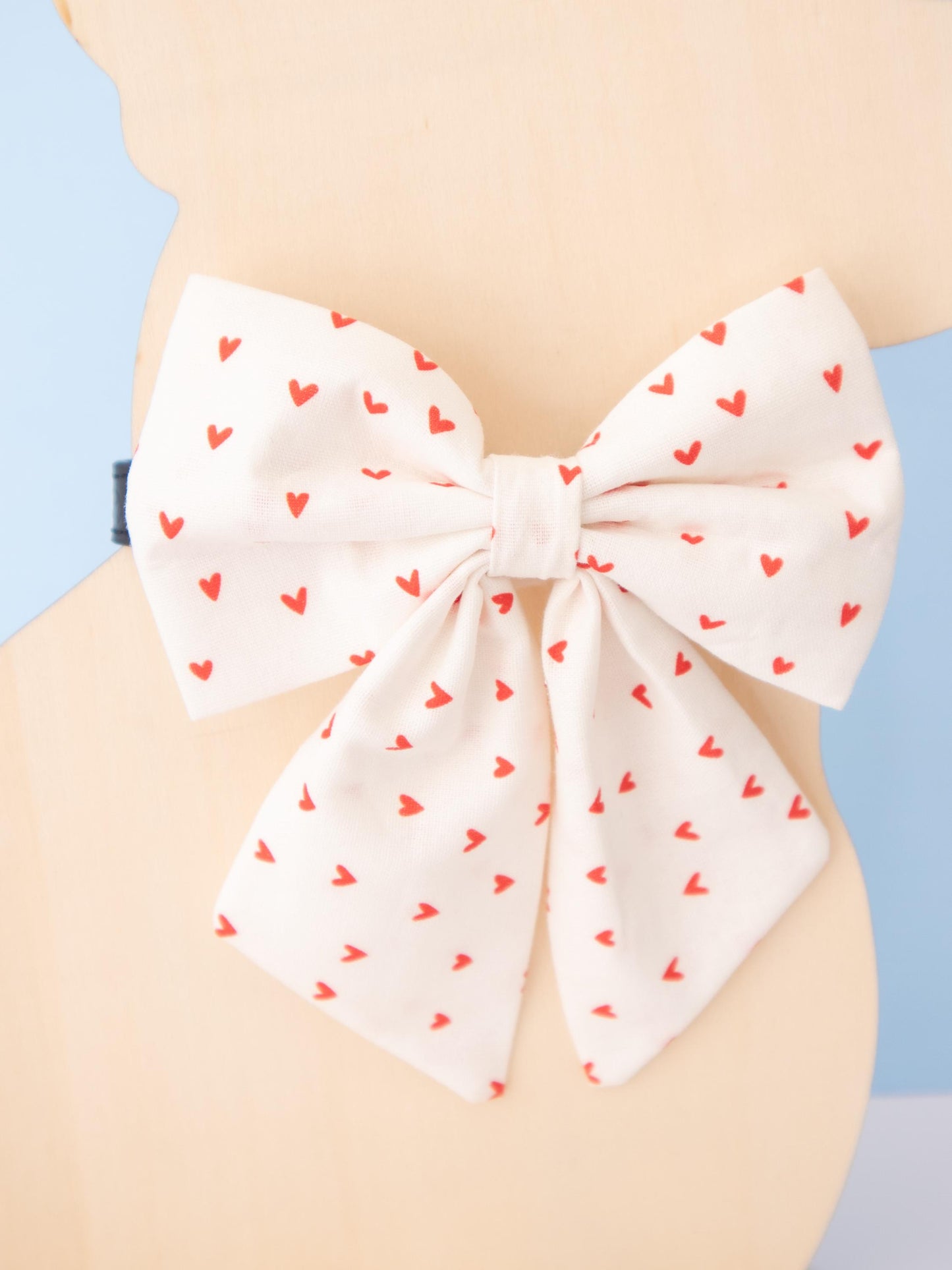 Dog Mannequin wearing a large white bow with red heart patterns on a light blue background