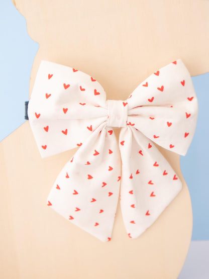 Dog Mannequin wearing a large white bow with red heart patterns on a light blue background