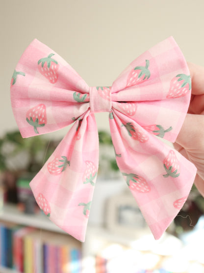Pink bow with strawberry pattern held by a hand against a blurred background
