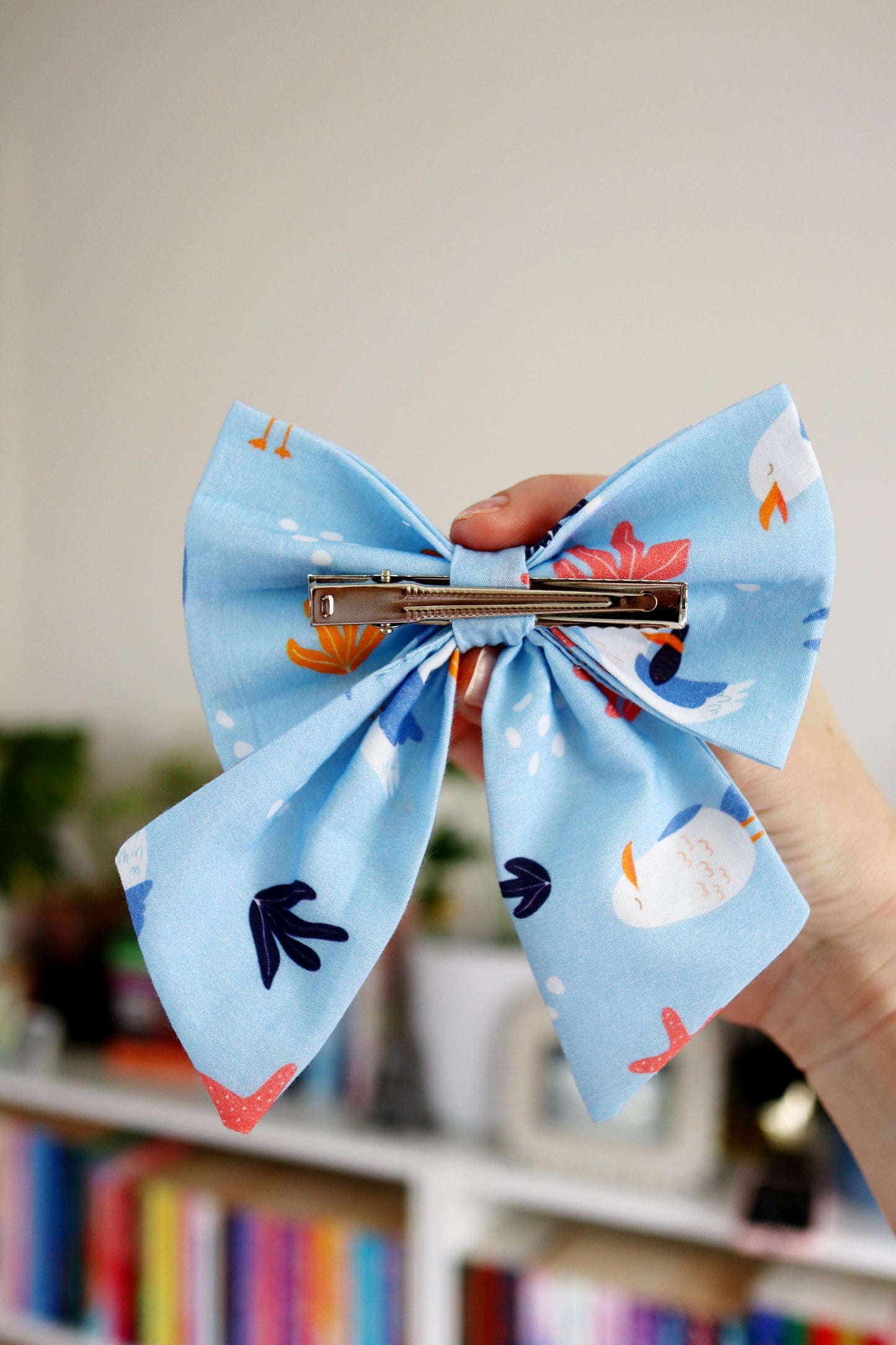Large blue bow with cartoon character design held by a hand against a blurred indoor background