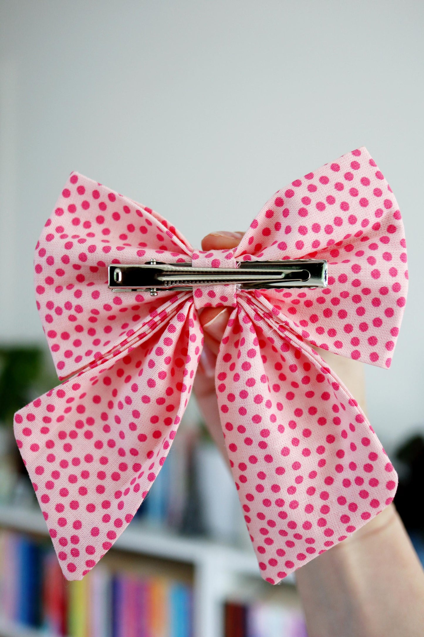 Pink polka dot bow hair clip held by a hand against a blurred background