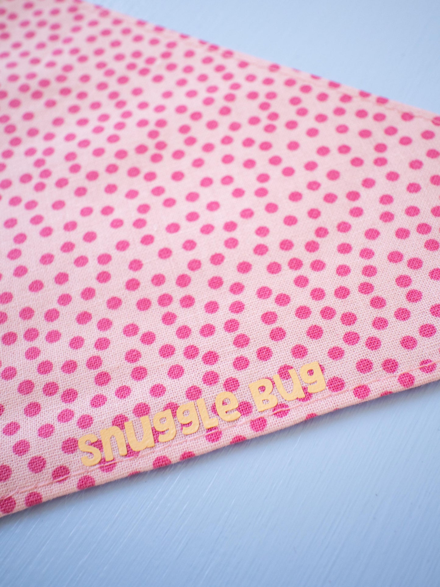 Pink polka dot bandana with 'snuggle bug' text on a light blue background