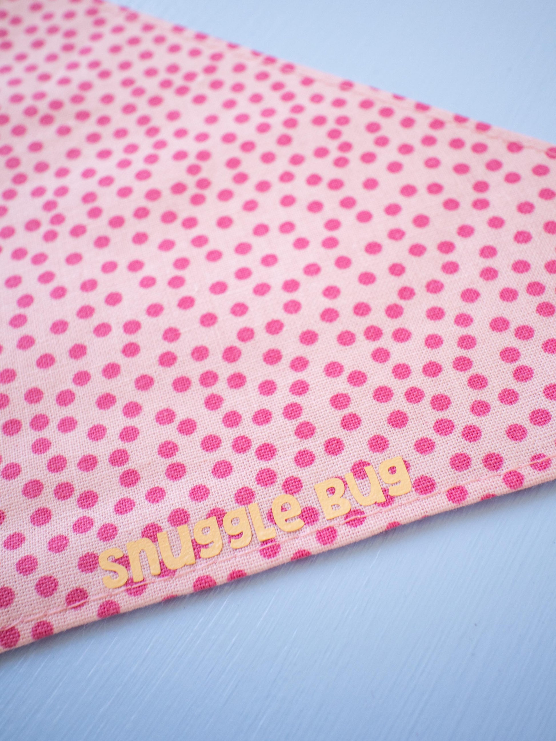 Pink polka dot bandana with 'snuggle bug' text on a light blue background