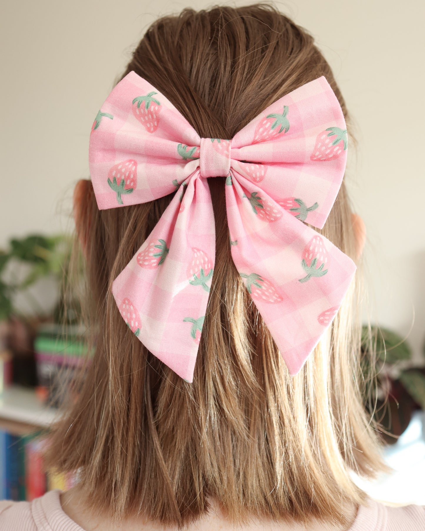 Person wearing a large pink hair bow with strawberry pattern in a casual setting