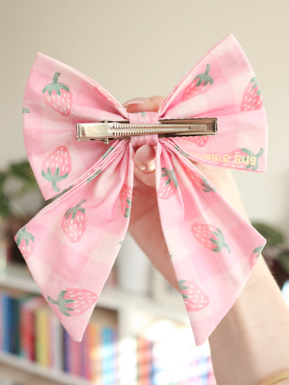 Large pink bow with strawberry pattern held by a hand against a blurred indoor background