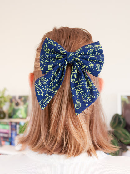 Navy blue bow with neon green space themed patterns on a person's head with a blurred indoor background