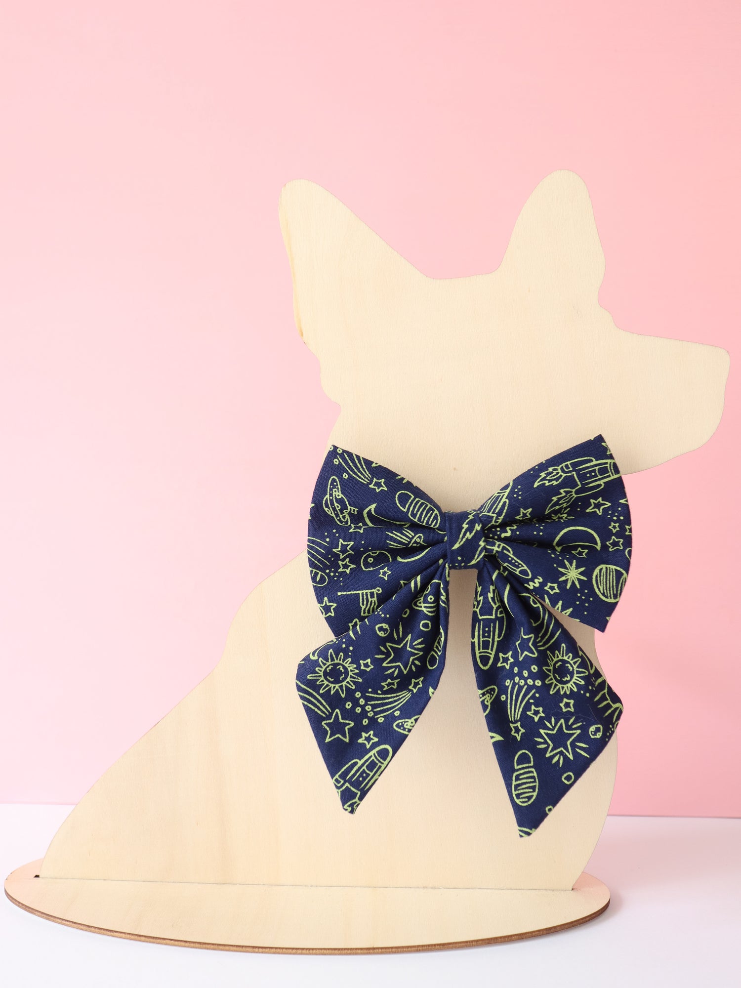 Navy blue bow with neon green space themed patterns on a white dog-shaped headband against a pink background