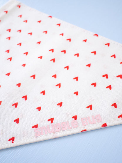 White dog bandana with red heart pattern and 'Snuggle Bug' branding on a light blue background