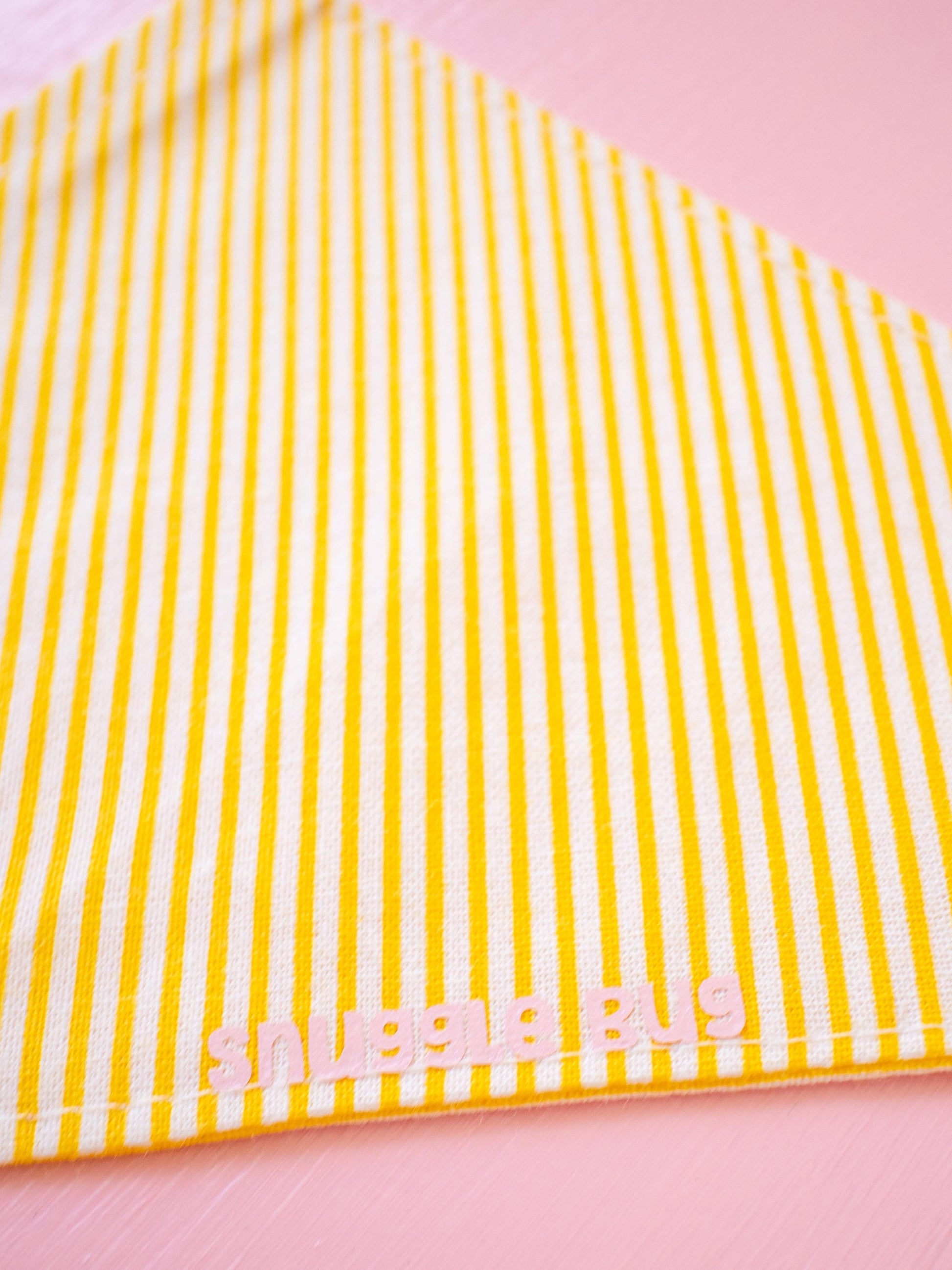 Yellow and white striped fabric with 'Snuggle Bug' branding on a pink background