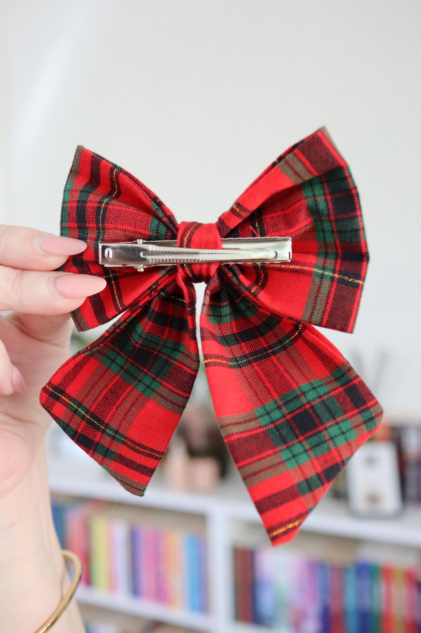 Red plaid bow hair clip held by a hand with a blurred background