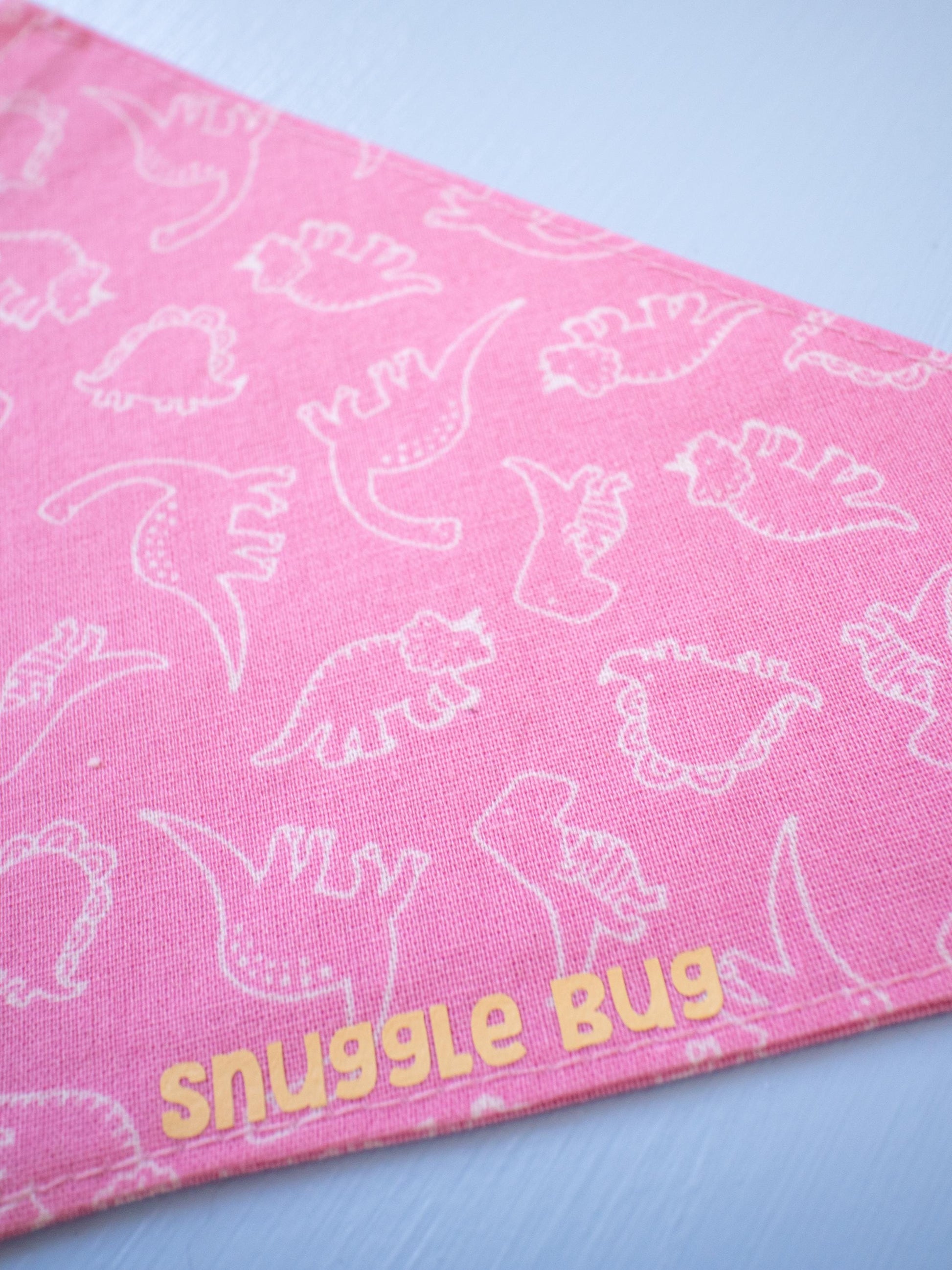 Pink bandana with white dinosaur patterns and 'snuggle bug' text on a light blue background