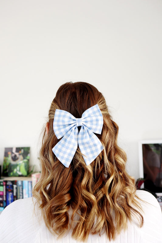 Person with wavy hair wearing a small blue checkered bow in the back against a white wall.