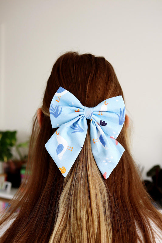 Person with a large blue bow in their hair against a neutral background