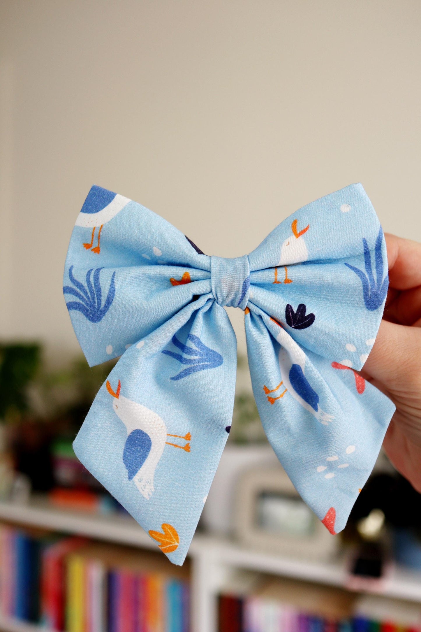 Blue bow with bird pattern held against a blurred indoor background